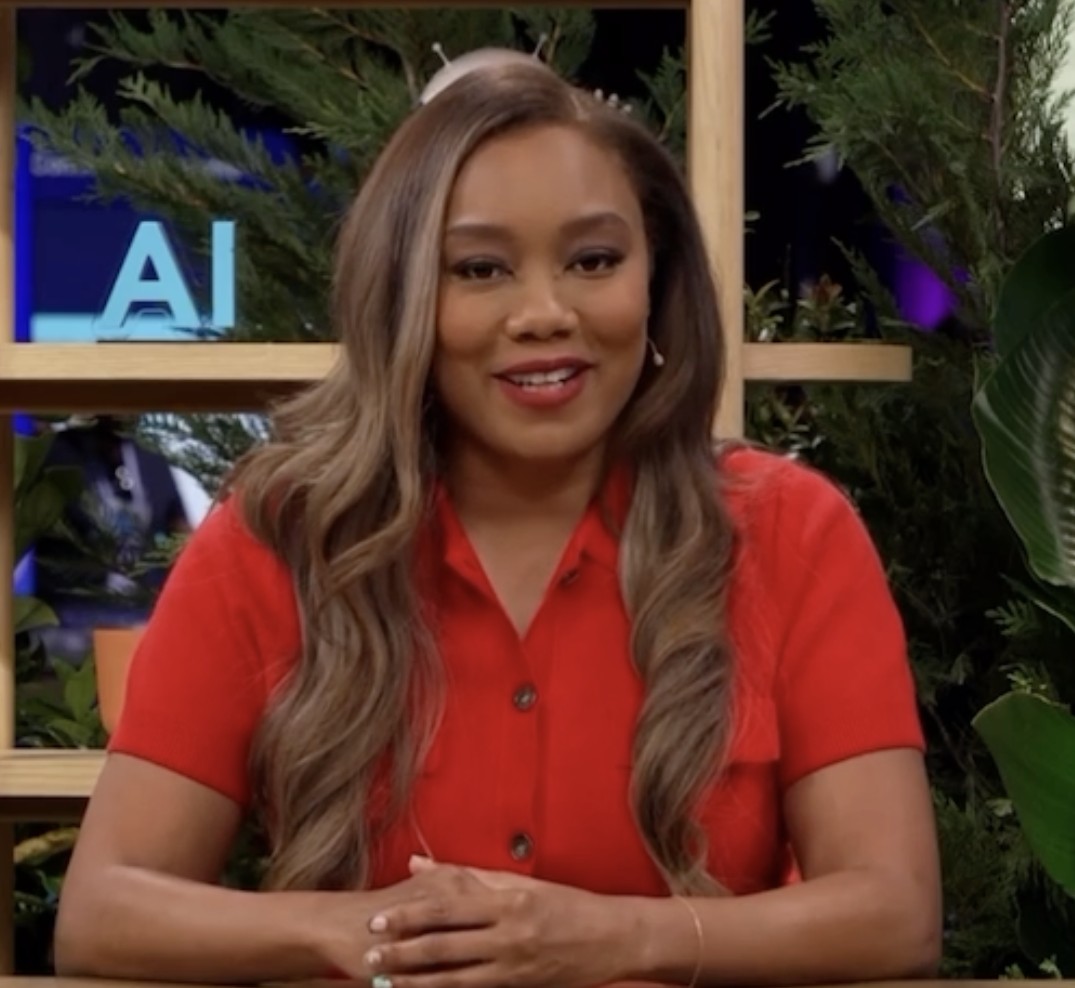 Monica Bowie seated at a studio anchor desk on a conference broadcast set
